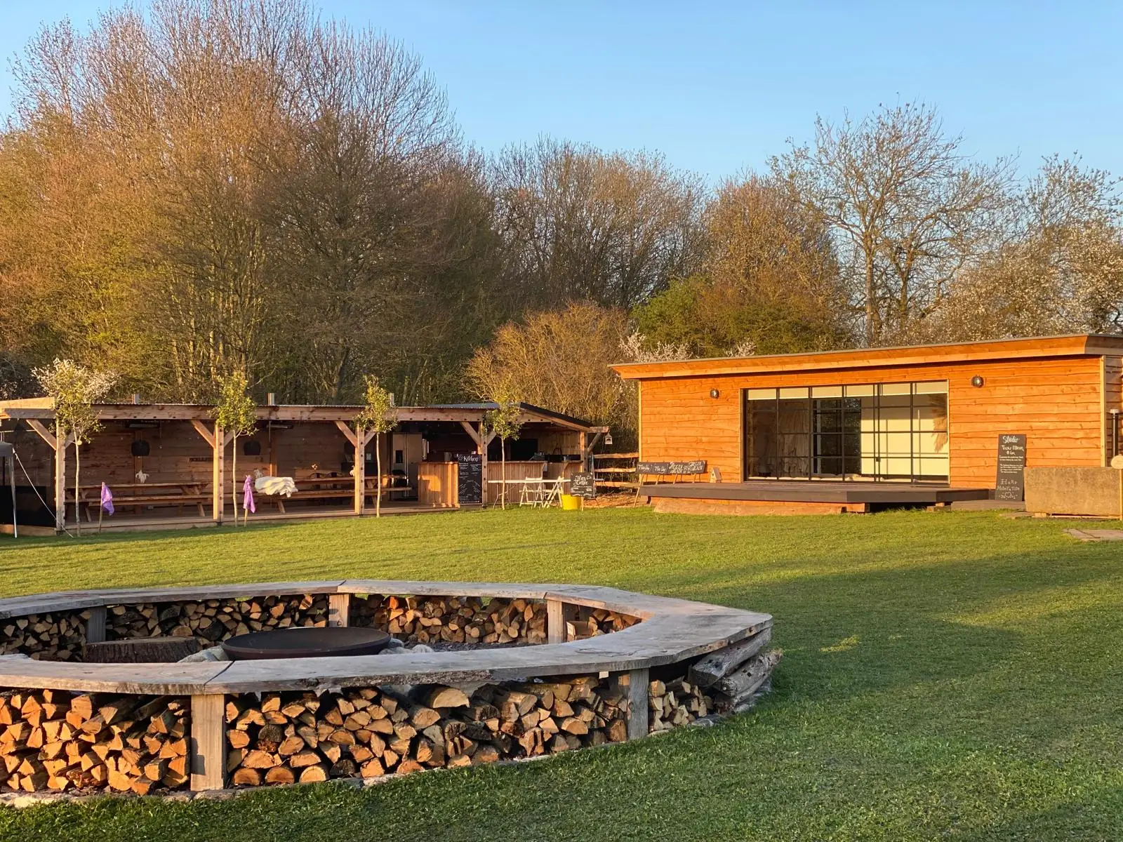 Fickle Field at golden hour — fire pit, log store and cabin in the Essex countryside