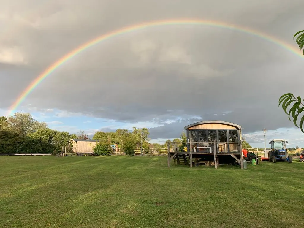 A rainbow over Fickle Field with the cabin and tractor in the foreground