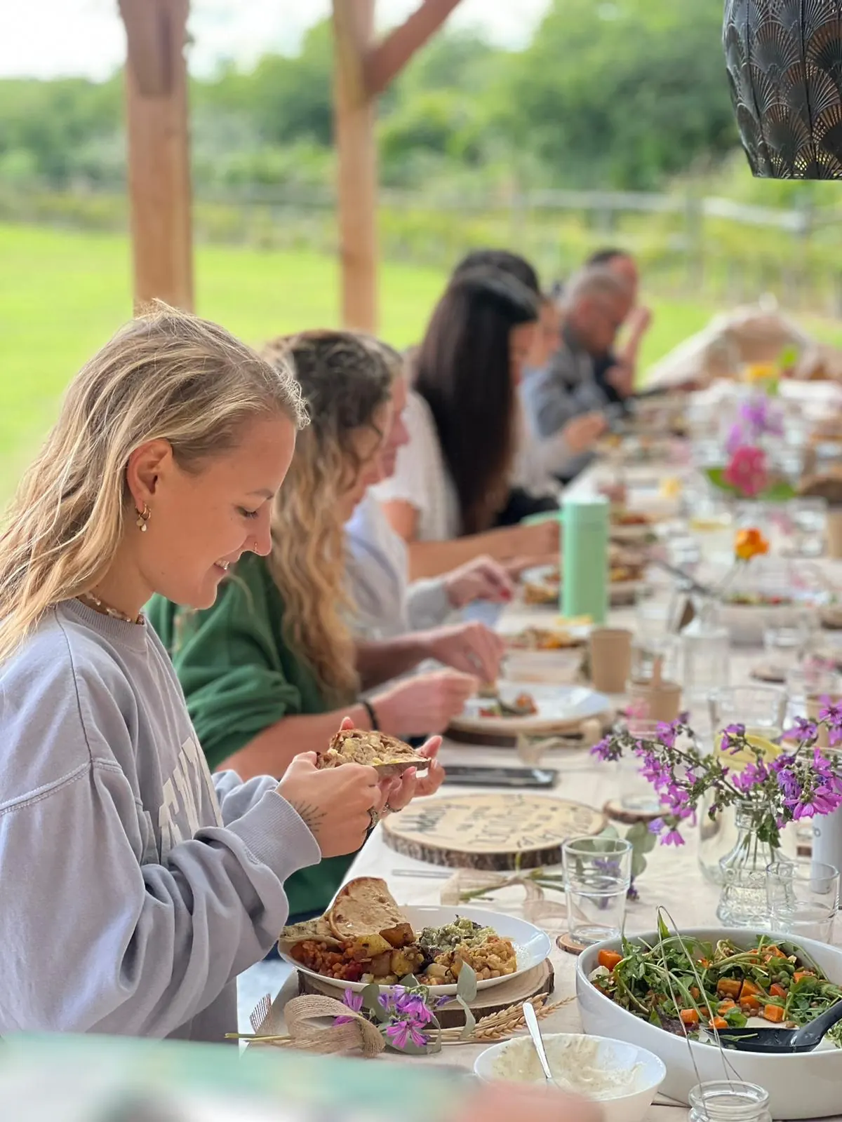 Long supper-club table with people eating and wildflowers